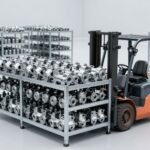 Container khung thép lớn chứa nhiều chi tiết kim loại giống nhau, xe nâng đứng bên cạnh trong trung tâm phân phối — ảnh bìa bài ISTA 3H