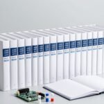 Dãy sách tiêu chuẩn dày không có chữ trên gáy đặt trên bàn cùng bo mạch điện tử, lọ mẫu và sổ tay đang mở — ảnh bìa bài IEC 62321